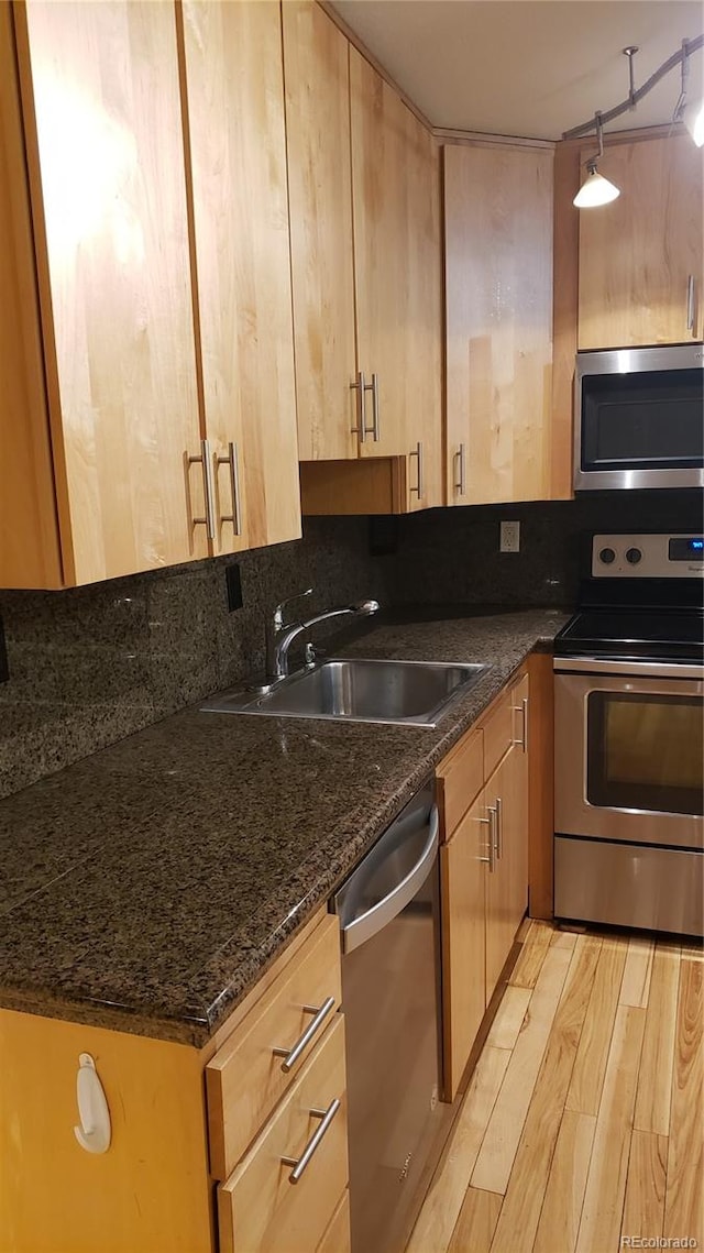 kitchen with dark stone counters, rail lighting, sink, appliances with stainless steel finishes, and light hardwood / wood-style flooring