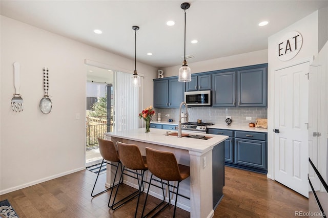 kitchen with pendant lighting, dark hardwood / wood-style floors, blue cabinets, and a kitchen island with sink