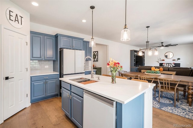 kitchen with a center island with sink, blue cabinetry, hanging light fixtures, and light hardwood / wood-style flooring