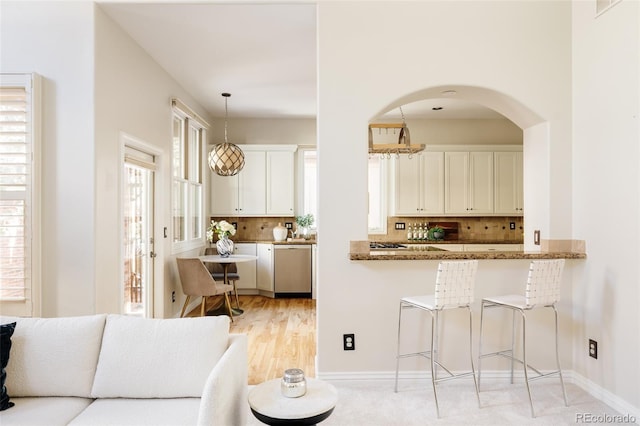 kitchen with dishwasher, pendant lighting, decorative backsplash, kitchen peninsula, and light stone countertops