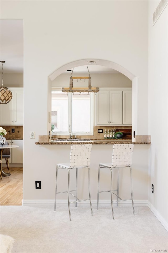 kitchen with light colored carpet, white cabinets, tasteful backsplash, and stone countertops