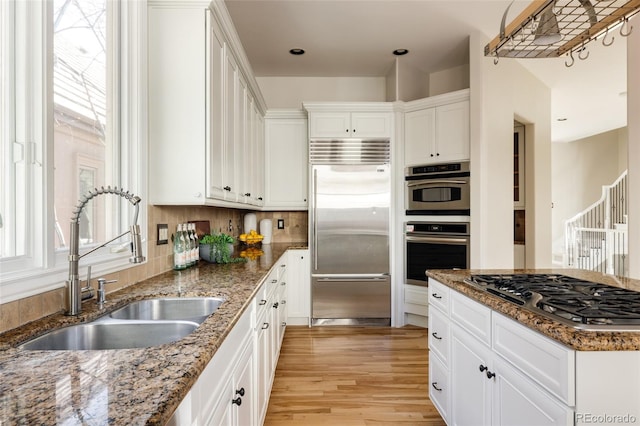 kitchen with appliances with stainless steel finishes, sink, white cabinetry, and dark stone counters