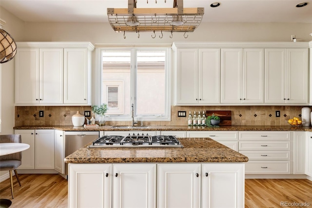 kitchen featuring a center island, white cabinetry, stainless steel appliances, dark stone countertops, and backsplash