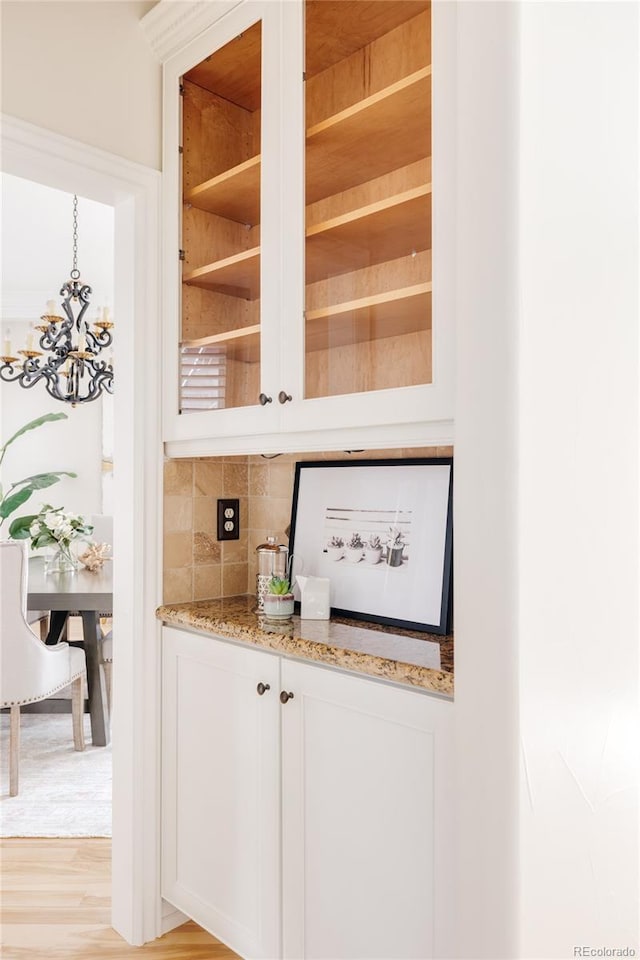 bar with pendant lighting, white cabinetry, an inviting chandelier, light hardwood / wood-style floors, and light stone counters