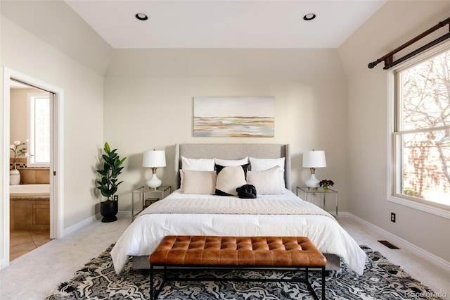 bedroom featuring ensuite bathroom, light carpet, and lofted ceiling