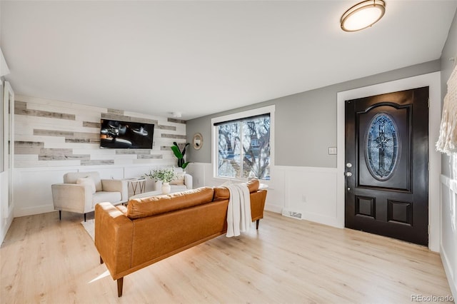 living area featuring light wood-style floors, an accent wall, visible vents, and a wainscoted wall