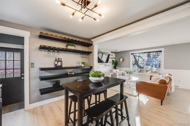 dining area with light wood finished floors, an inviting chandelier, and wainscoting