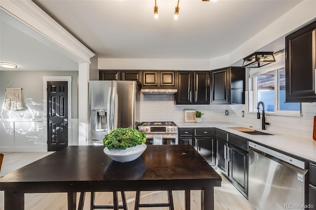 kitchen with stainless steel appliances, tasteful backsplash, light countertops, a sink, and under cabinet range hood