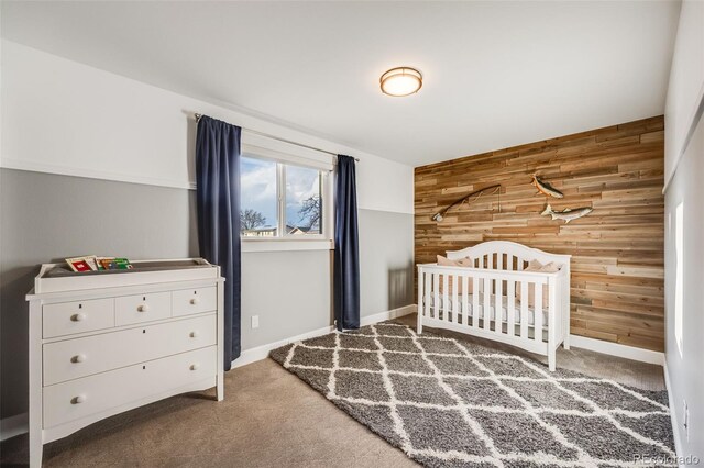 unfurnished bedroom with an accent wall, carpet flooring, wood walls, a crib, and baseboards