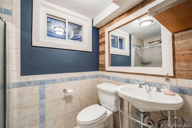 bathroom with a stall shower, tile walls, wainscoting, toilet, and a sink