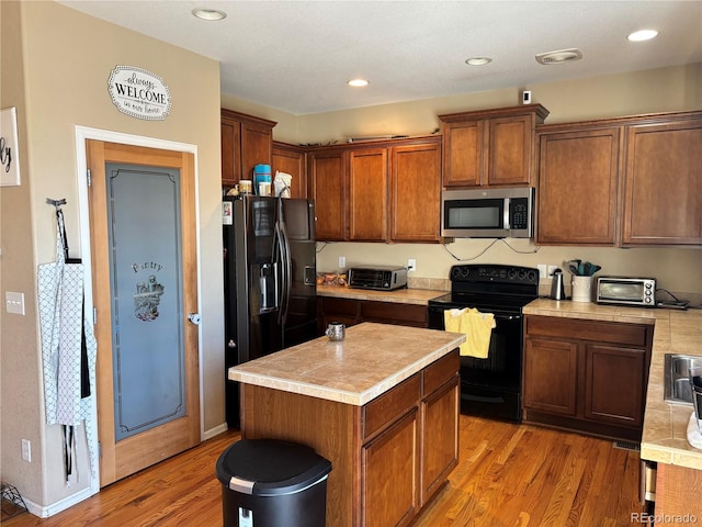 kitchen with light wood-type flooring, black appliances, and a kitchen island