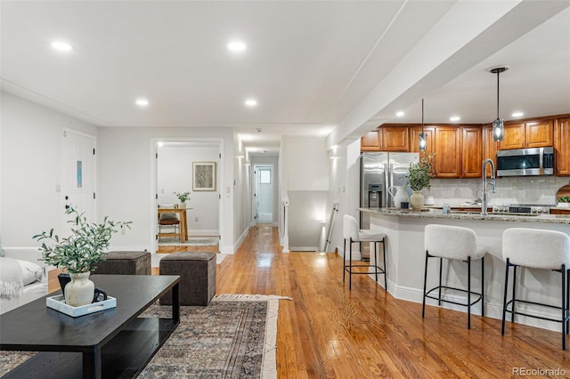 kitchen featuring appliances with stainless steel finishes, hanging light fixtures, a kitchen breakfast bar, light hardwood / wood-style floors, and light stone countertops