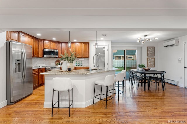 kitchen with sink, appliances with stainless steel finishes, an island with sink, a wall unit AC, and pendant lighting