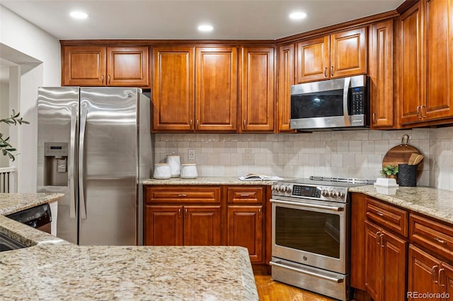 kitchen with appliances with stainless steel finishes, light hardwood / wood-style flooring, light stone counters, and decorative backsplash