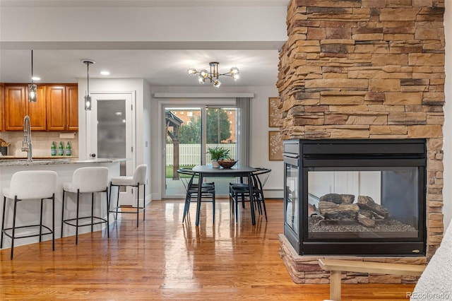 kitchen with sink, a breakfast bar area, hanging light fixtures, backsplash, and light hardwood / wood-style floors