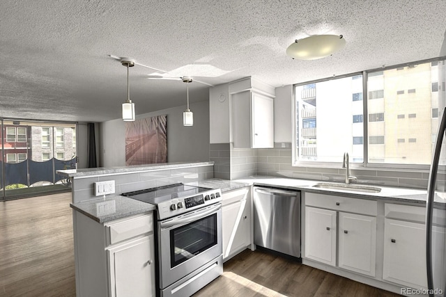 kitchen featuring dark wood-type flooring, a peninsula, stainless steel appliances, white cabinetry, and a sink