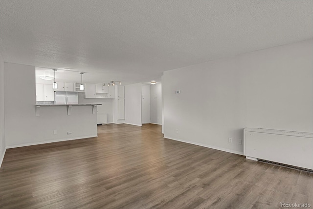 unfurnished living room with a textured ceiling, dark wood-style flooring, and baseboards