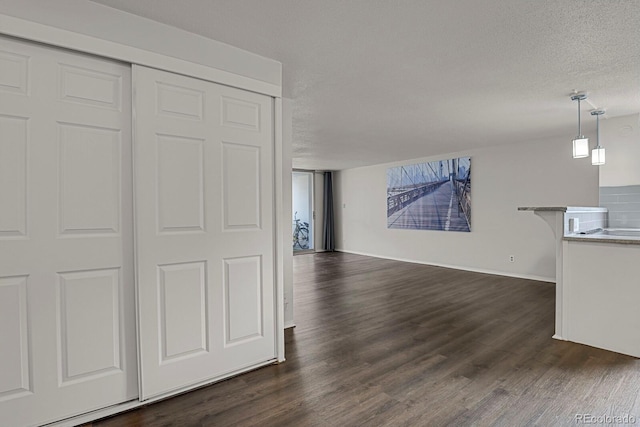 unfurnished living room with a textured ceiling, baseboards, and dark wood-style flooring