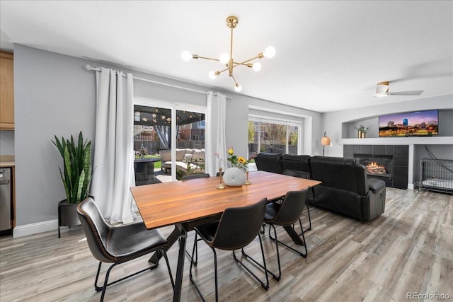 2153 Mountain Iris Dr, Erie, CO 80516 - dining area with light wood-style flooring, a chandelier, a fireplace, a ceiling fan, and baseboards