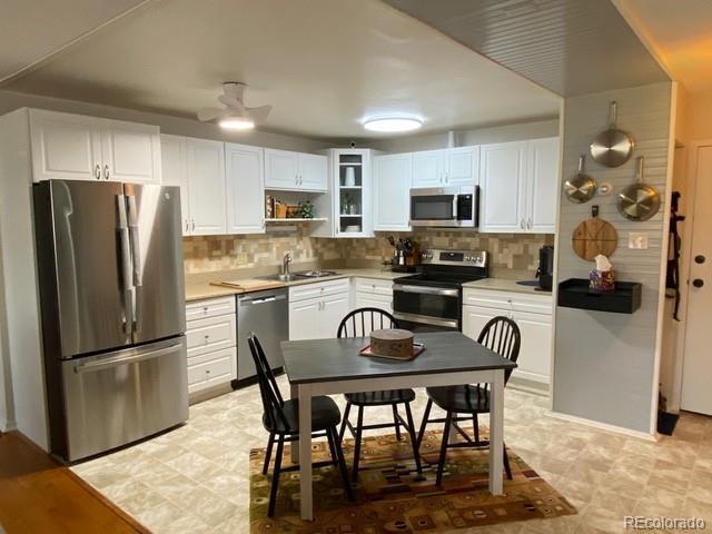 kitchen with a ceiling fan, stainless steel appliances, light countertops, white cabinets, and backsplash