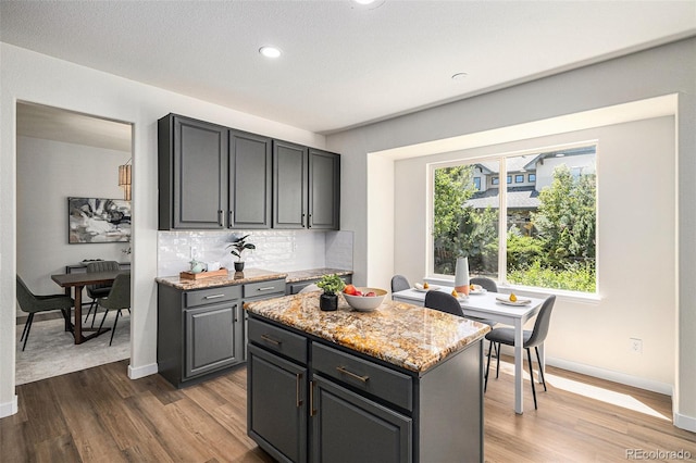 11868 W Progress Ave, Littleton, CO 80127 - kitchen with wood finished floors, decorative backsplash, light stone countertops, a center island, and recessed lighting