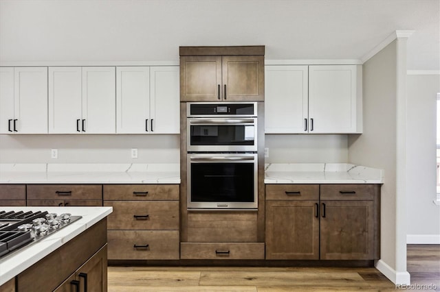 kitchen featuring crown molding, light stone countertops, light hardwood / wood-style floors, white cabinetry, and stainless steel appliances