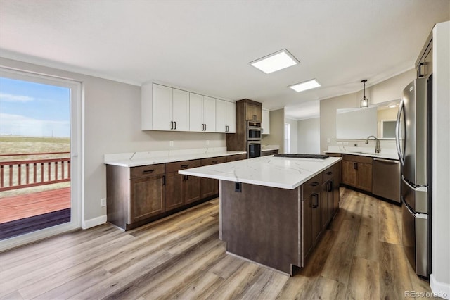 kitchen with white cabinetry, stainless steel appliances, decorative light fixtures, a kitchen island, and light wood-type flooring