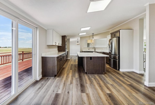 kitchen with dark wood-type flooring, stainless steel refrigerator with ice dispenser, decorative light fixtures, dark brown cabinets, and a kitchen island