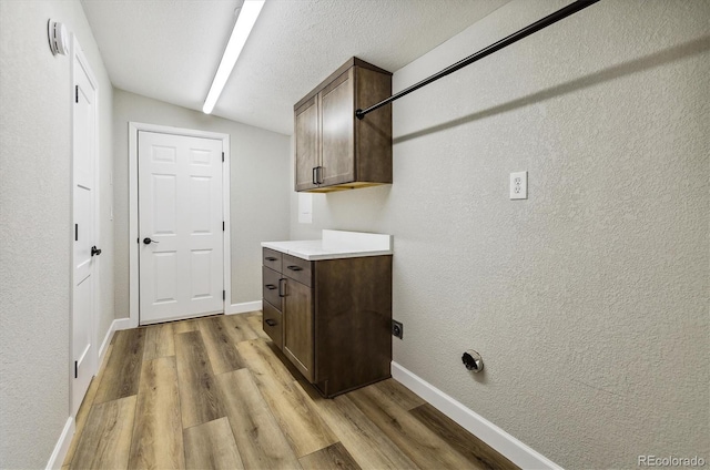 clothes washing area with cabinets, a textured ceiling, and light hardwood / wood-style floors