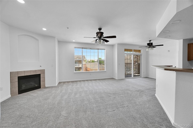 unfurnished living room with a tiled fireplace, light colored carpet, and ceiling fan