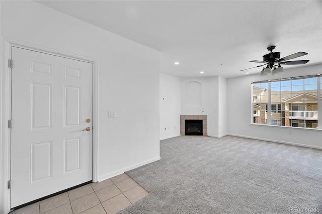 unfurnished living room featuring light carpet, a tiled fireplace, and ceiling fan