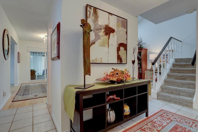 hall with light tile patterned floors, baseboards, stairway, and a textured ceiling