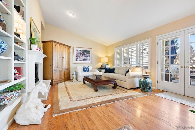 living area featuring lofted ceiling, a fireplace with raised hearth, french doors, and wood finished floors