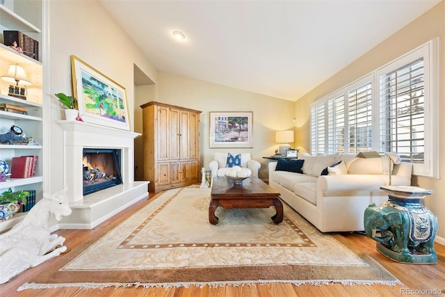 living room with lofted ceiling, a glass covered fireplace, baseboards, and wood finished floors