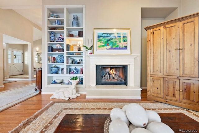 living room with built in shelves, a lit fireplace, baseboards, and wood finished floors