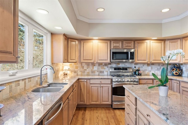 kitchen with light stone counters, stainless steel appliances, a sink, light wood-type flooring, and crown molding