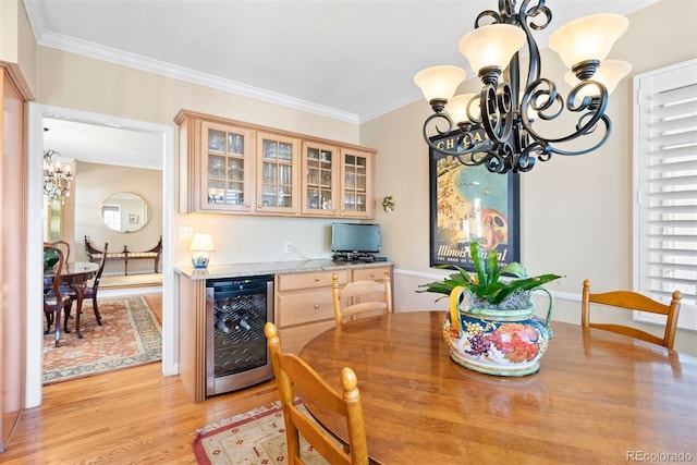 dining area with a dry bar, light wood-style flooring, wine cooler, crown molding, and a chandelier