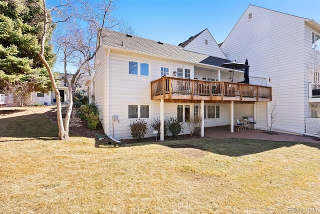 back of house featuring a shingled roof, a lawn, a patio area, and a wooden deck