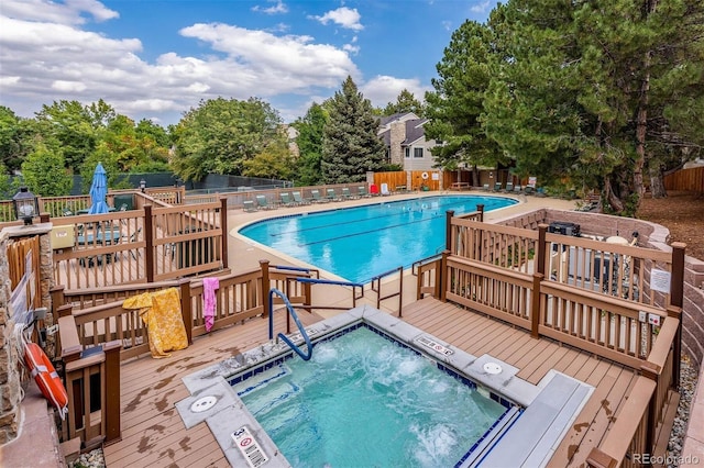 pool with fence, a wooden deck, and a hot tub