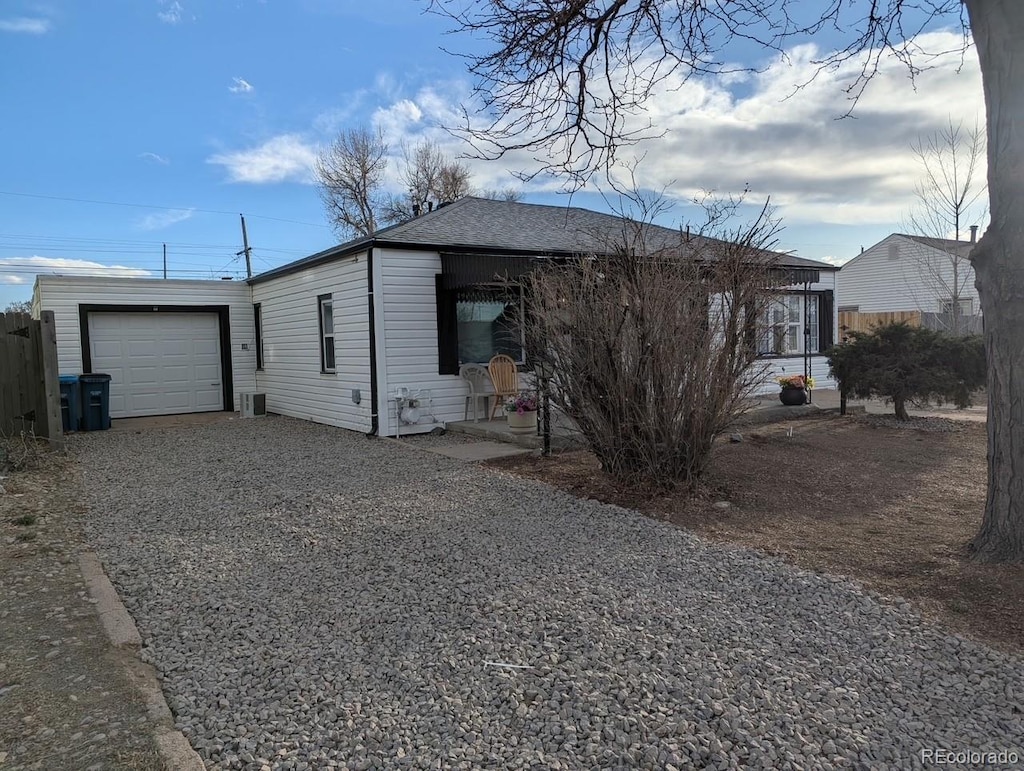 view of side of property with a shingled roof, gravel driveway, a garage, and fence