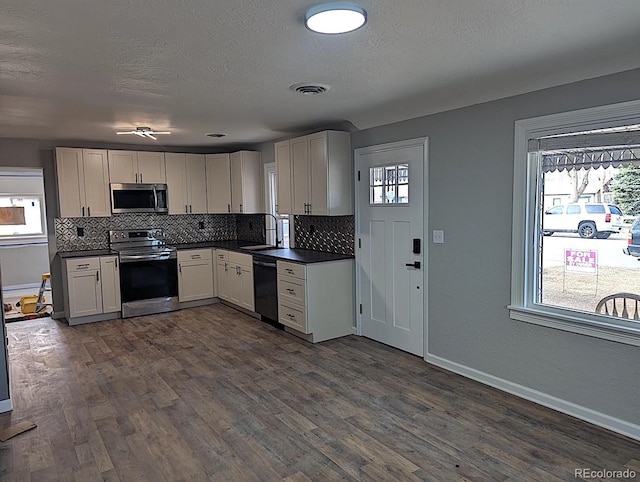 kitchen with a sink, dark countertops, backsplash, stainless steel appliances, and dark wood-style flooring