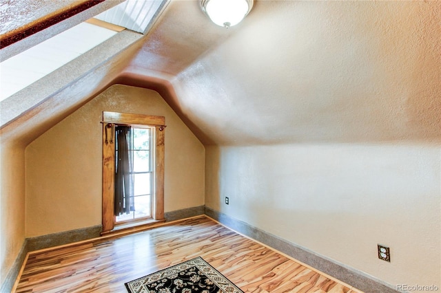 additional living space with a textured ceiling, light hardwood / wood-style flooring, and lofted ceiling with skylight