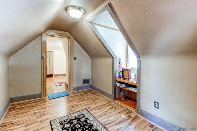 additional living space featuring a textured ceiling, light hardwood / wood-style floors, and lofted ceiling