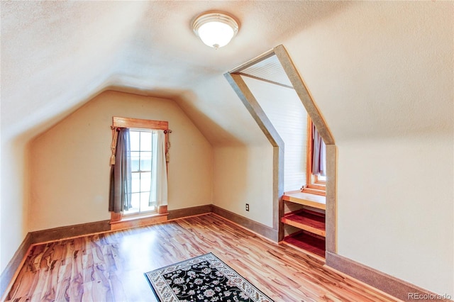 additional living space featuring a textured ceiling, light hardwood / wood-style flooring, and vaulted ceiling