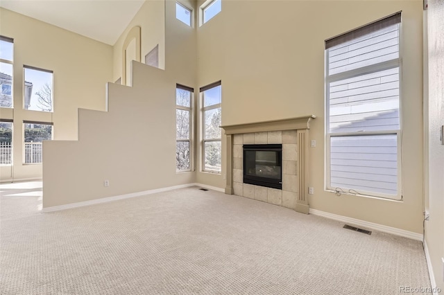 unfurnished living room featuring carpet floors, a towering ceiling, visible vents, baseboards, and a tiled fireplace