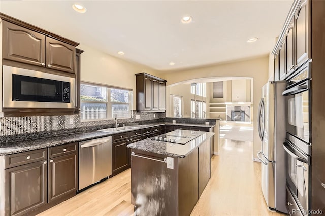 kitchen featuring a fireplace, stainless steel appliances, tasteful backsplash, a sink, and dark brown cabinetry