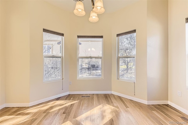 unfurnished dining area featuring an inviting chandelier, visible vents, baseboards, and wood finished floors