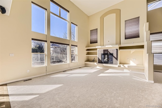 unfurnished living room featuring visible vents, a high ceiling, carpet, and a high end fireplace