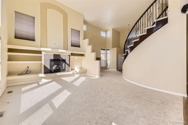 unfurnished living room featuring baseboards, a tiled fireplace, stairway, a high ceiling, and carpet floors