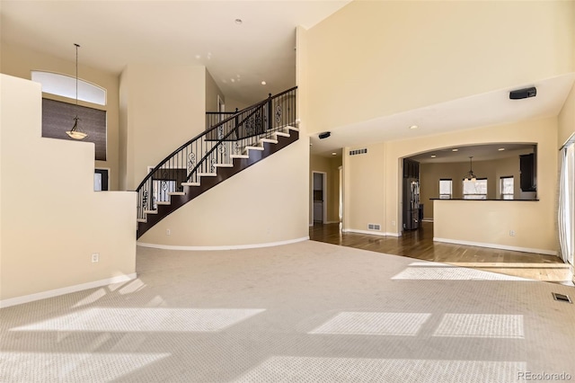 unfurnished living room with carpet, visible vents, a high ceiling, baseboards, and stairs